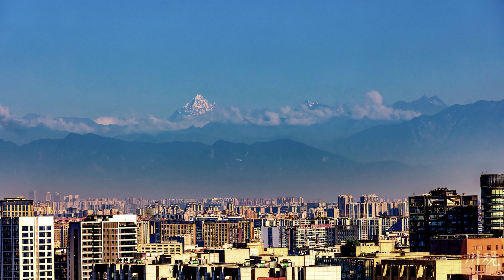 7月19日清晨，澄澈晴空下，成都城区连片楼宇与远处雪山清晰同框。C视觉签约摄影师 青健 摄